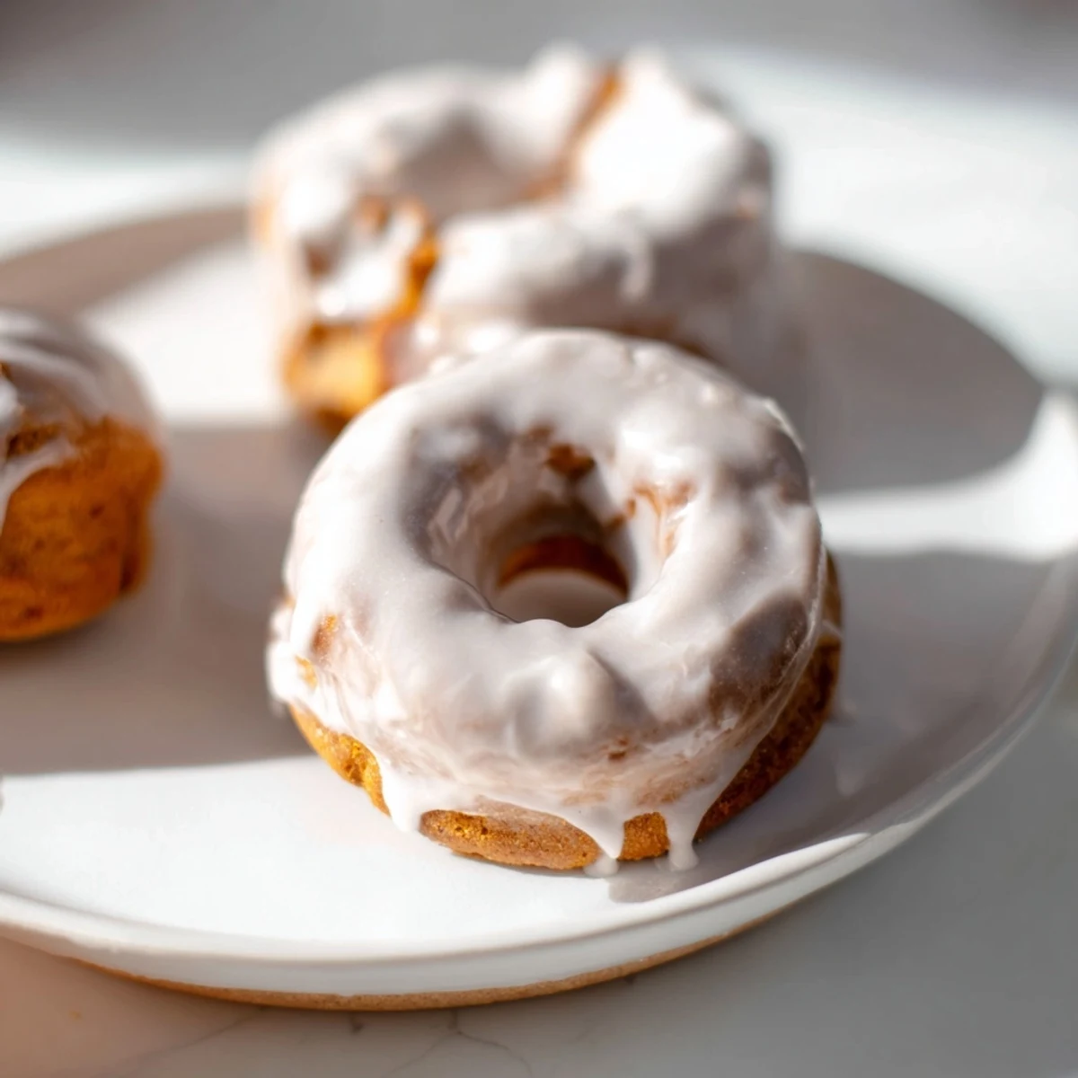 Chewy gluten-free pumpkin mochi donuts drizzled with rich maple frosting on a white plate