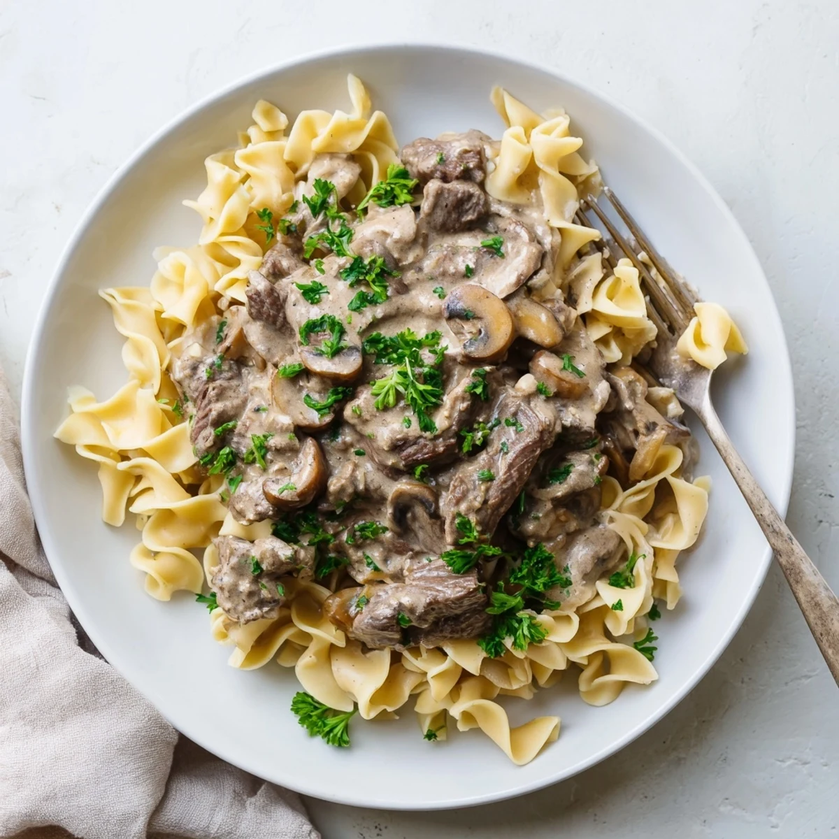 Homemade beef and mushroom stroganoff plated on white noodles with chopped parsley topping