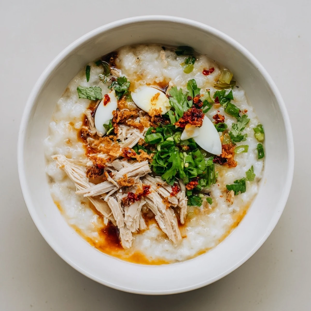 Creamy leftover Thanksgiving turkey congee topped with fresh scallions, cilantro, and a drizzle of chili oil in a white bowl.