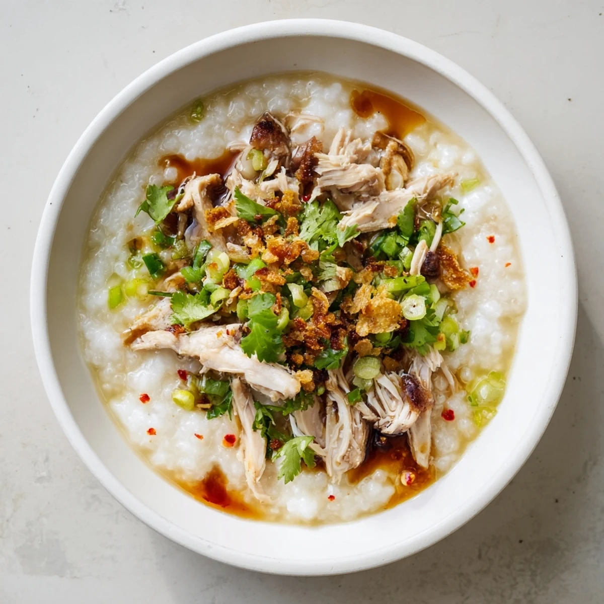 Steaming bowl of savory turkey congee with shredded meat, ginger, and crispy shallots garnish on a wooden table.