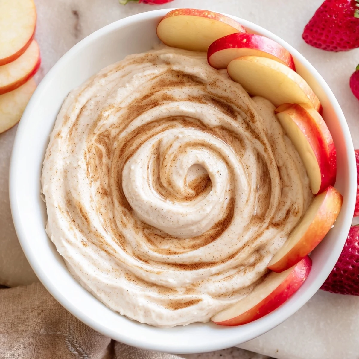 Creamy healthy Greek yogurt cinnamon roll dip swirled with cinnamon and surrounded by fresh apple slices and strawberries.