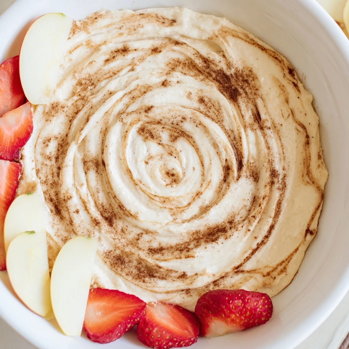 Wholesome Greek yogurt cinnamon roll dip with marbled cinnamon topping displayed alongside banana slices and orange segments for dipping.