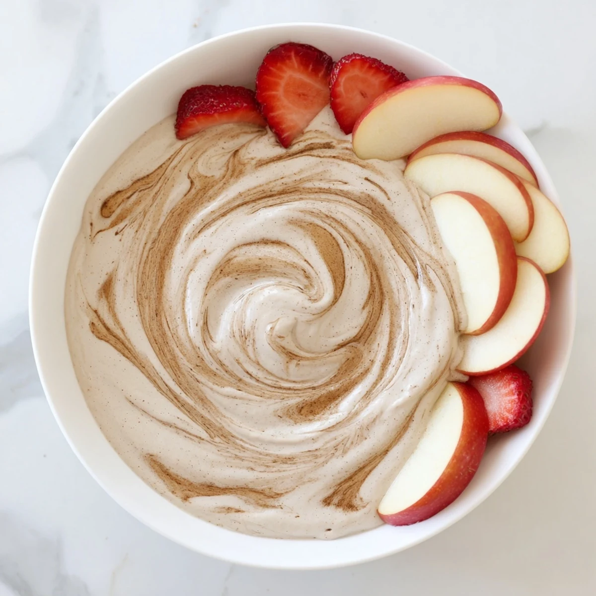 Protein-packed Greek yogurt cinnamon roll dip topped with cinnamon swirl and served with pear slices and grapes on a platter.