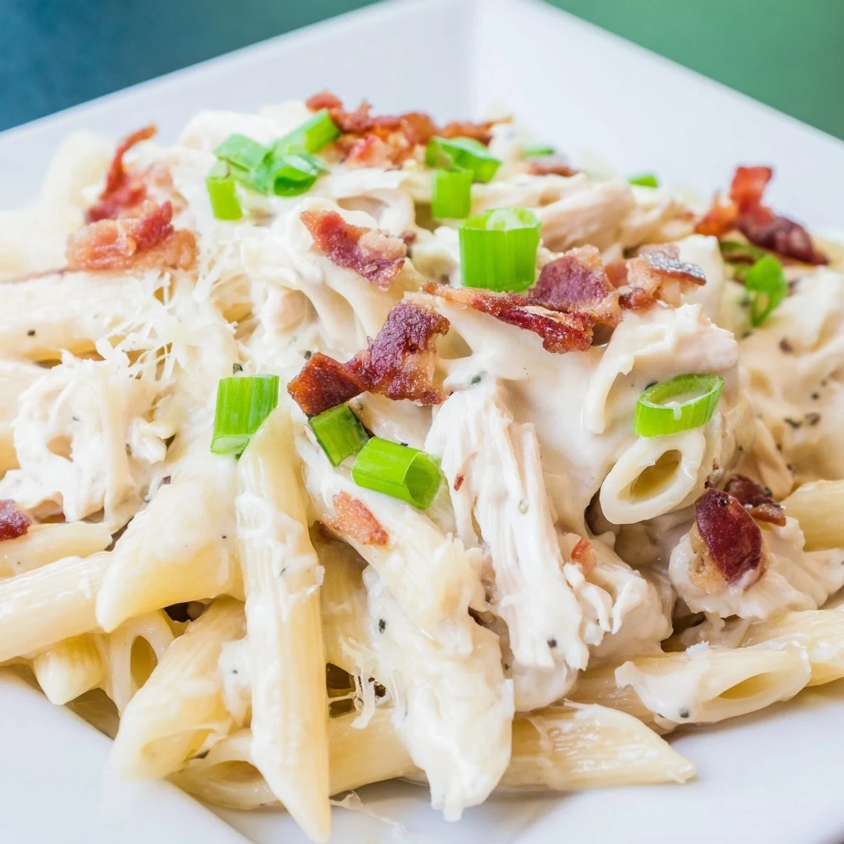 Steaming plate of crack chicken pasta featuring shredded chicken, bacon bits, and melted parmesan cheese