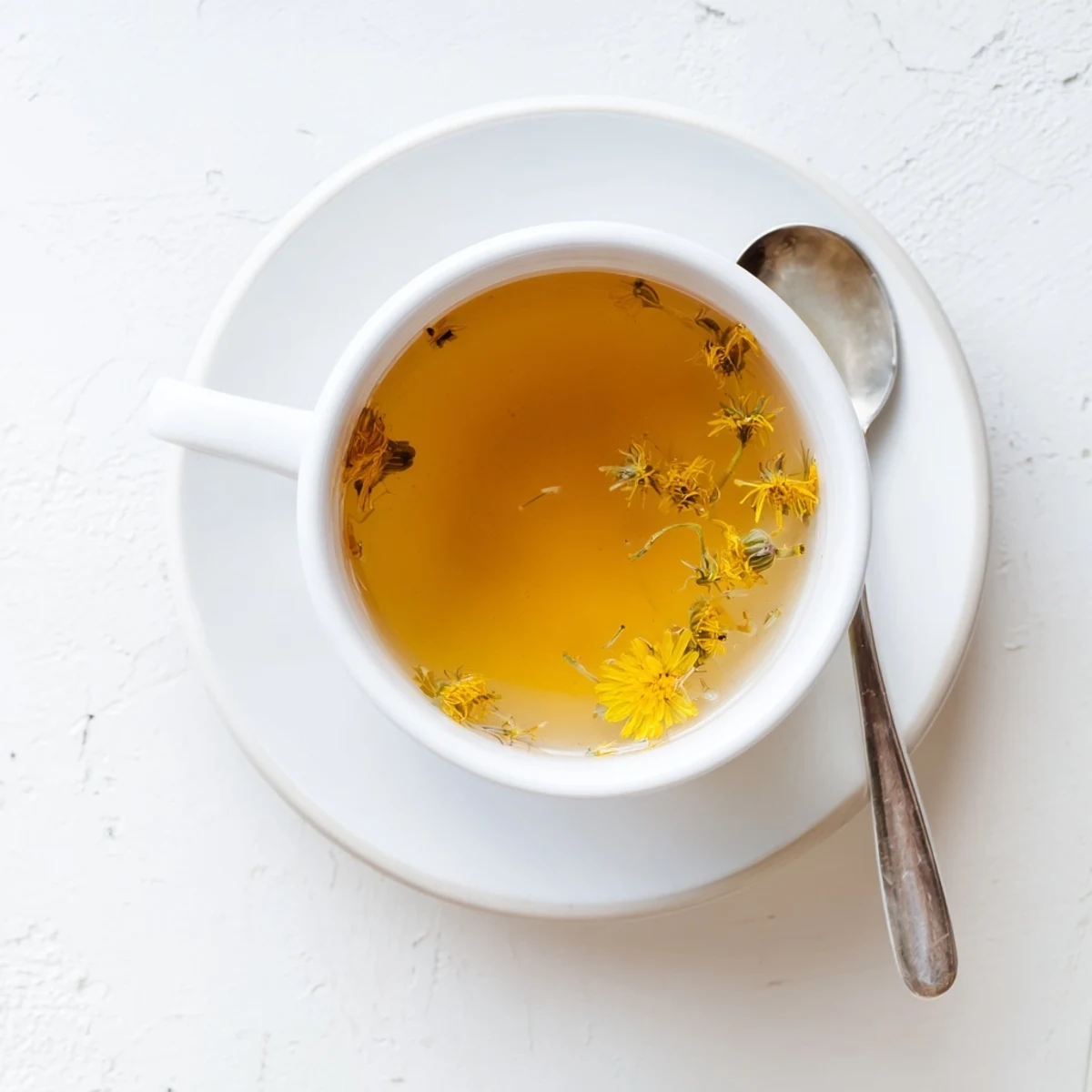 Golden amber dandelion tea steaming in a white ceramic teacup with fresh petals floating atop