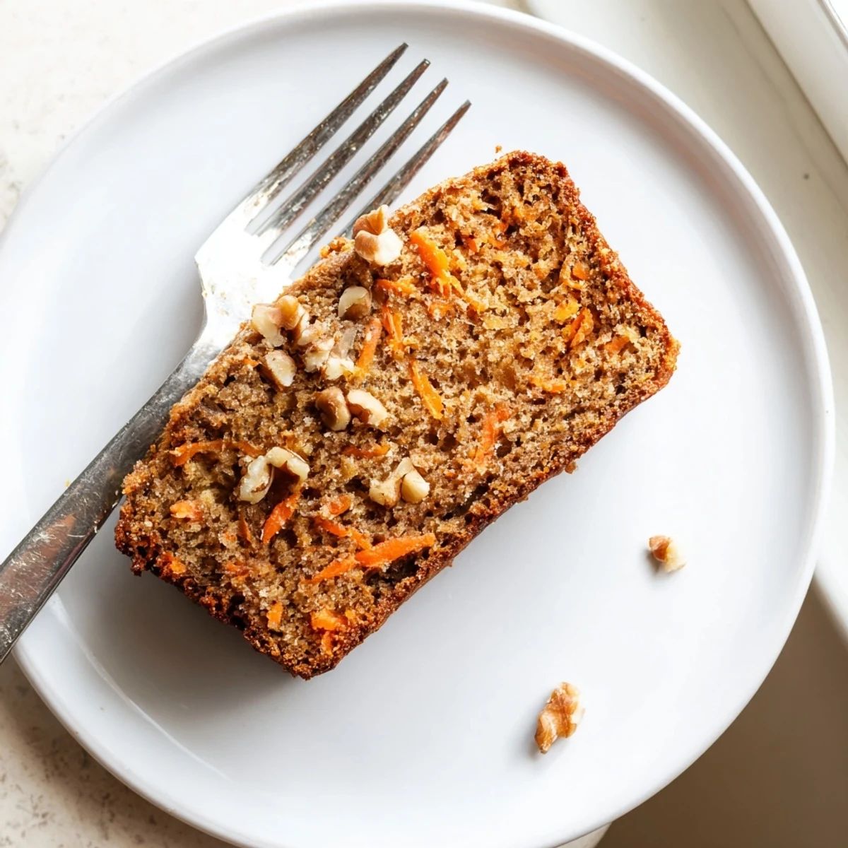 Golden brown carrot cake banana bread loaf topped with chopped walnuts on a wooden cutting board