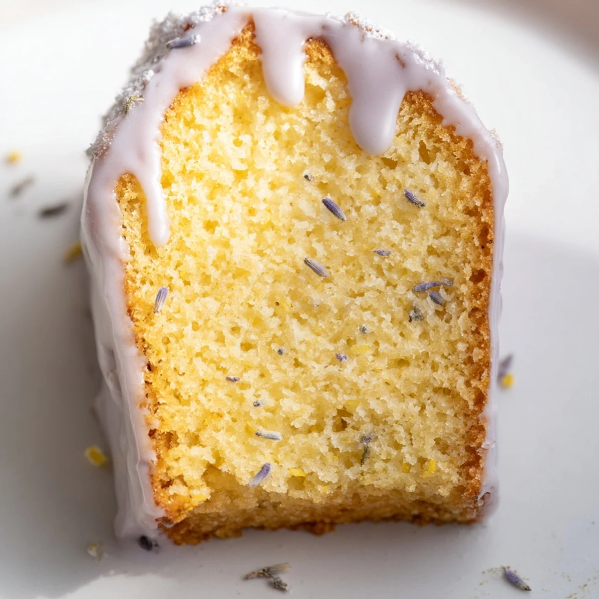 Soft lavender cake slice topped with sweet citrus icing on white plate