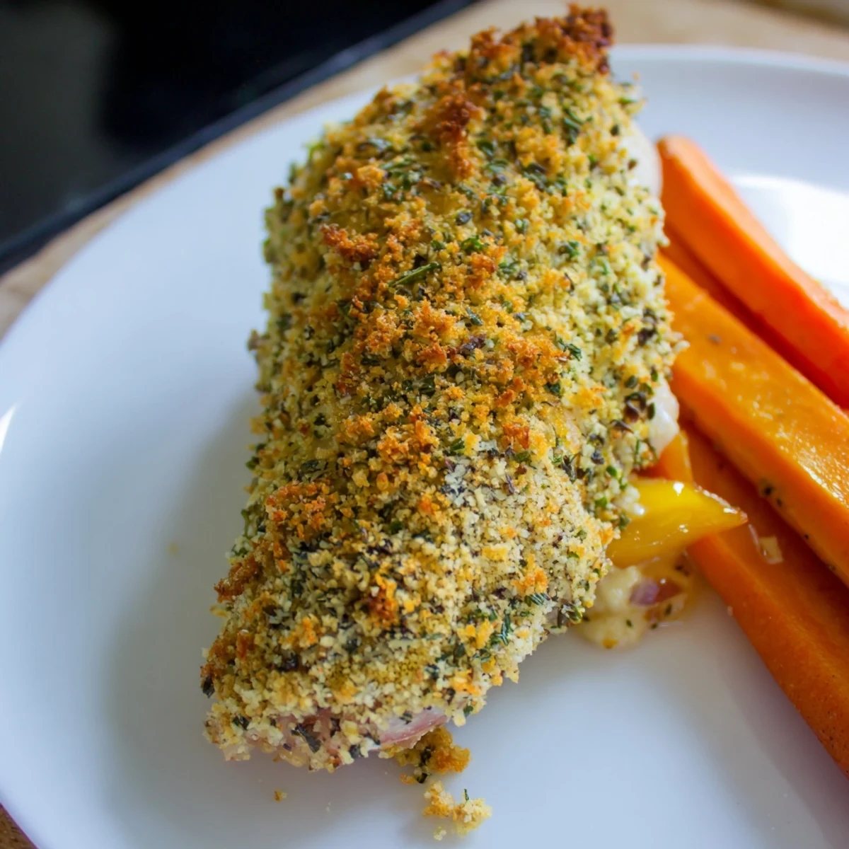 Juicy baked chicken with aromatic parsley and thyme crust on a white plate with caramelized bell peppers and carrots