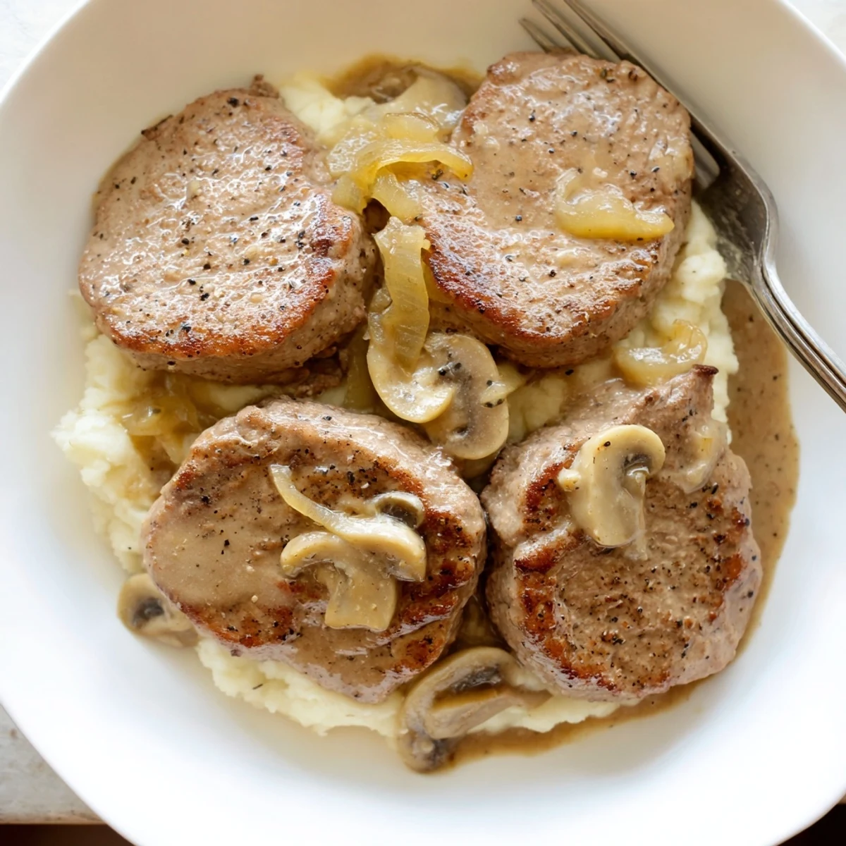 Sliced Country Style Smothered Cube Steak plated over creamy mashed potatoes, savory aroma