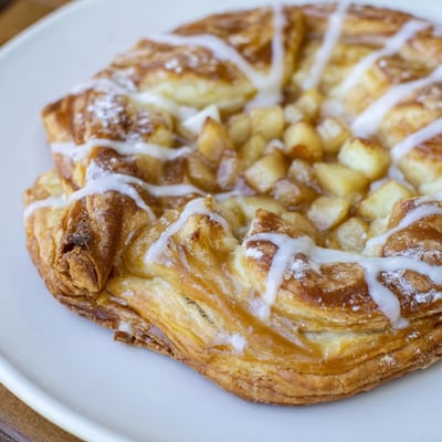 Flaky Apple Cheese Danishes drizzled with icing on a rustic parchment lined baking sheet